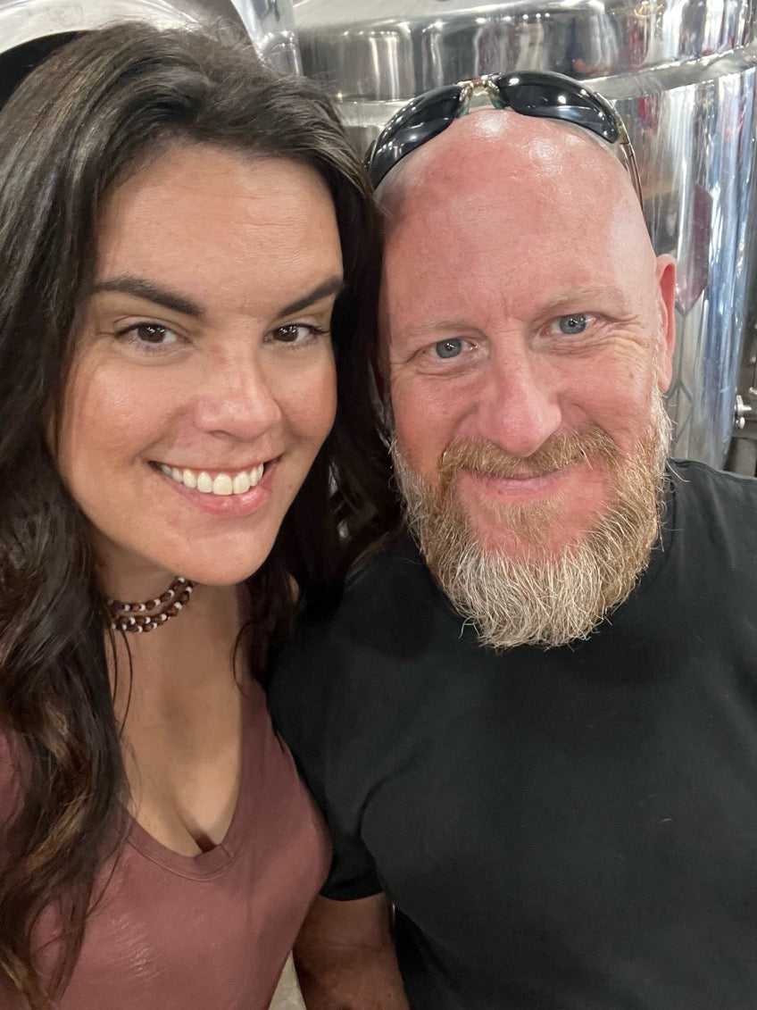 Two people posing together with a reflective surface in the background